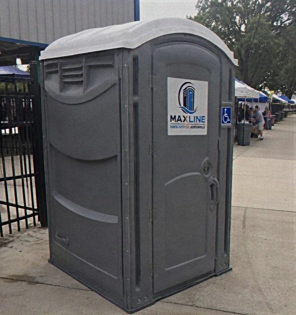 ADA-accessible portable toilet at an outdoor market with vendor tents behind