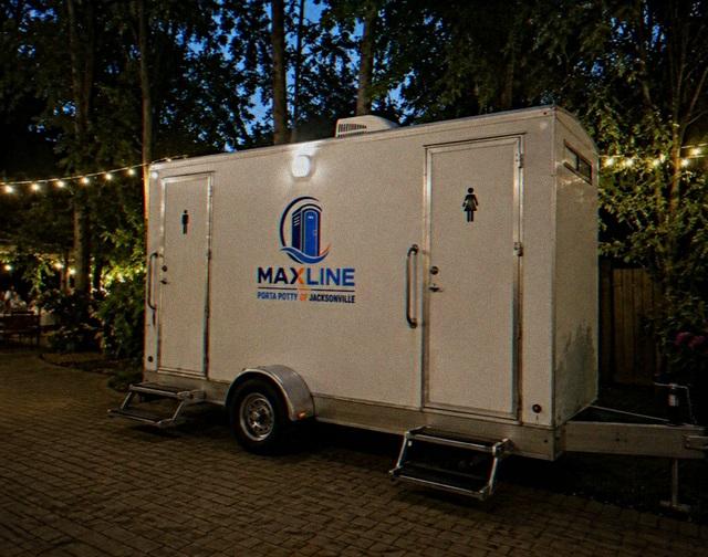 Lit two-stall Maxline restroom trailer at an evening event under string lights